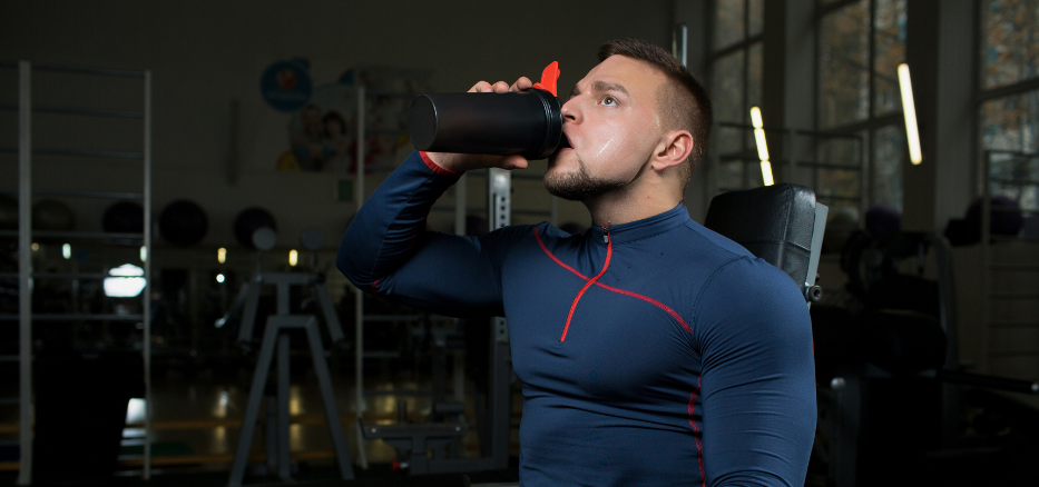 Mann på et treningsstudio som drikker fra sin shaker